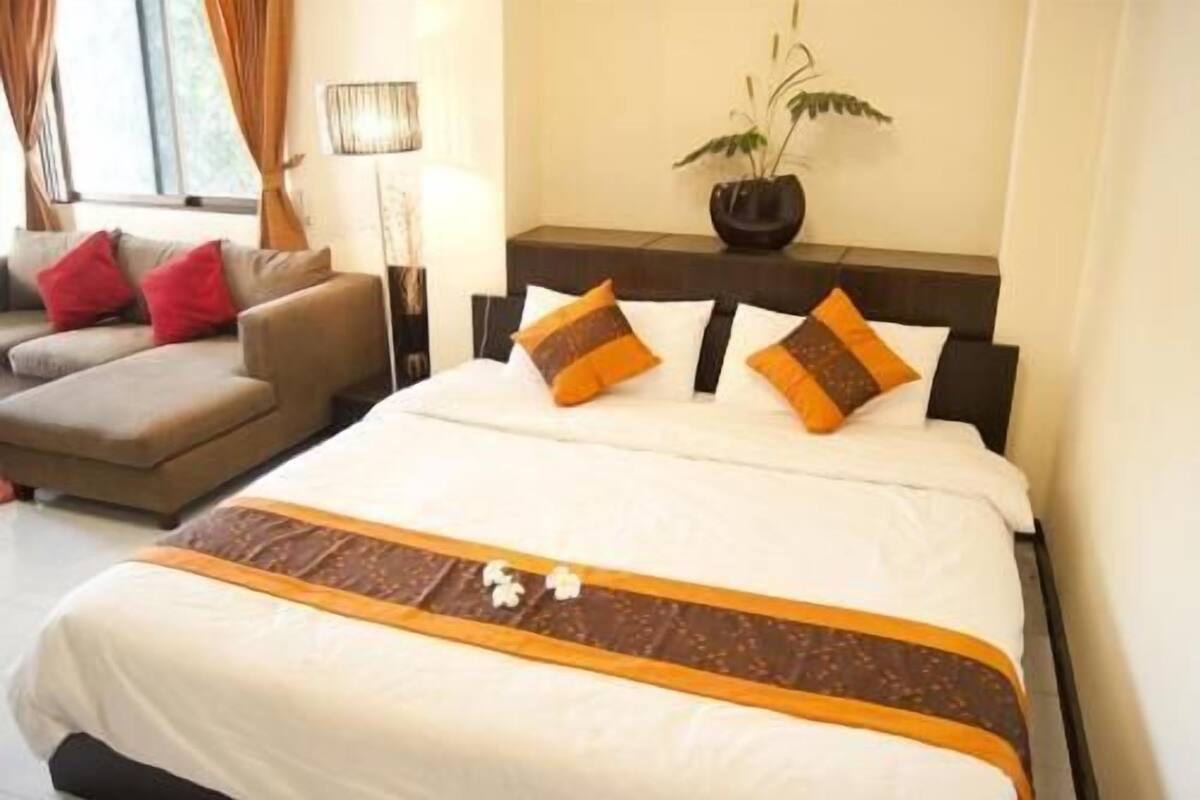 A hotel room with a bed, a sofa, a lamp, and a plant.