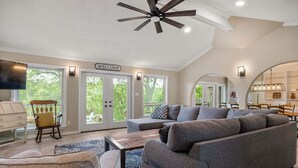 Ein geräumiges Wohnzimmer mit einem großen, grauen Ecksofa, einem Holzwippenstuhl, einem Couchtisch und einem Deckenventilator.