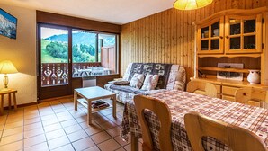 A cozy room with a bed, a table, and a chair, a wooden cabinet, and a view of a green landscape through a window. - Lovely apartment near ski slopes and village, pets allowed (La Clusaz)