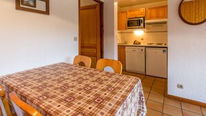A small kitchen with wooden cabinets, a microwave, and a dishwasher. There is a dining table with a checkered tablecloth and two chairs. - Lovely apartment near ski slopes and village, pets allowed (La Clusaz)