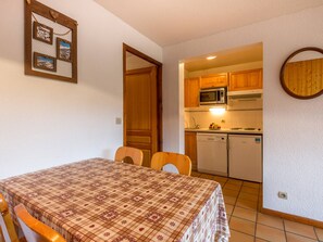 Cozinha compacta com armários de madeira, micro-ondas e lava-louças. Há uma mesa de jantar com toalha xadrez e duas cadeiras.