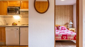 A compact kitchen with a microwave, dishwasher, and a fruit bowl on the counter. A wooden-framed mirror hangs on the wall. - Lovely apartment near ski slopes and village, pets allowed (La Clusaz)