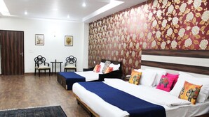 Habitación de hotel con dos camas, suelo de madera, papel tapiz floral y una pequeña mesa con sillas.