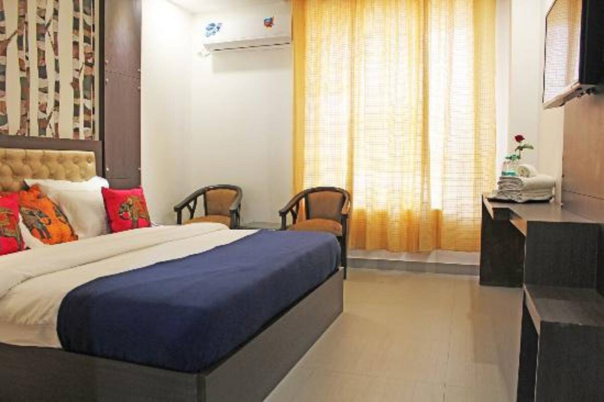 Una habitación de hotel con una cama, dos sillas, una mesita con toallas y una ventana con cortinas.