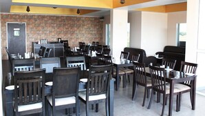 Un comedor con varias mesas y sillas, una pared de ladrillo y ventiladores de techo.