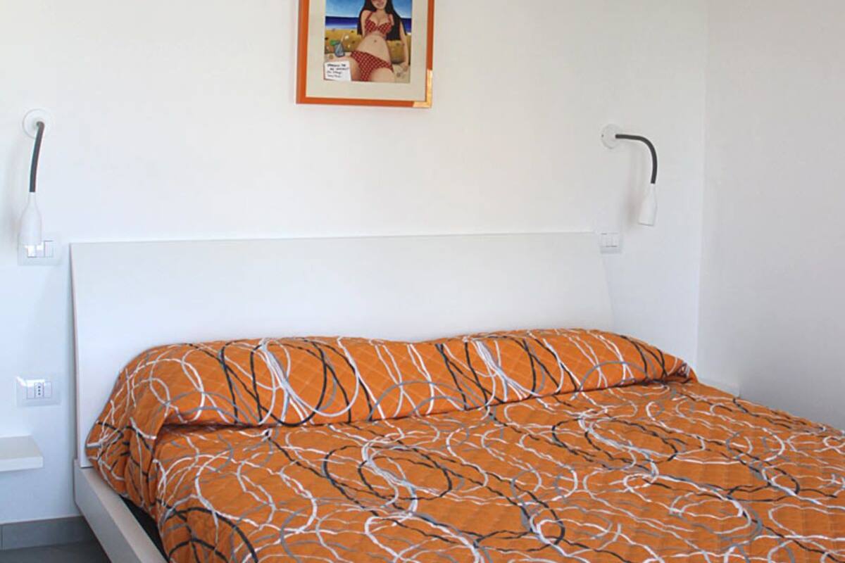 Una cama con un edredón naranja estampado, un cabecero blanco y un cuadro en la pared.