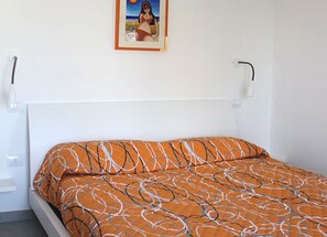 A bed with an orange patterned bedspread, a white headboard, and a framed picture on the wall.