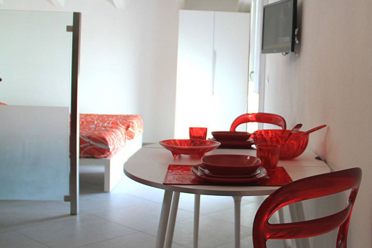 Comedor con una mesa redonda, sillas rojas y vajilla roja.