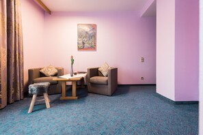 Una habitación con dos sofás, una mesita, un jarrón con una flor y un cuadro en la pared.