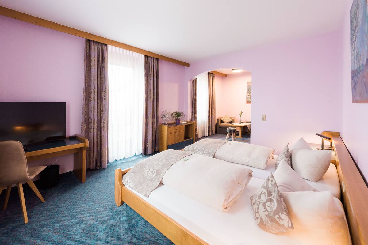 Quarto de hotel com cama, escrivaninha, cadeira, televisão e janela com cortinas.