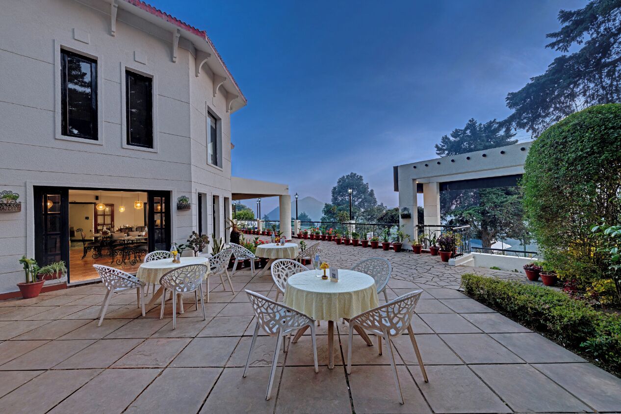 Una terrazza esterna con tavoli e sedie rotonde, l'ingresso di un edificio e piante in vaso.