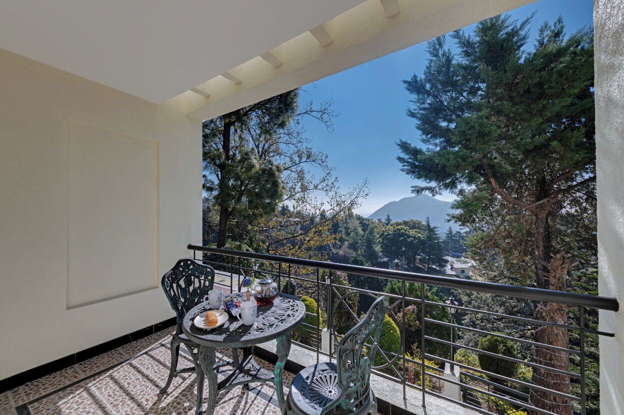 Un balcón con una mesa lista para dos personas, con vista a un paisaje montañoso y árboles.