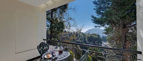 Un balcón con una mesa lista para dos personas, con vista a un paisaje montañoso y árboles.