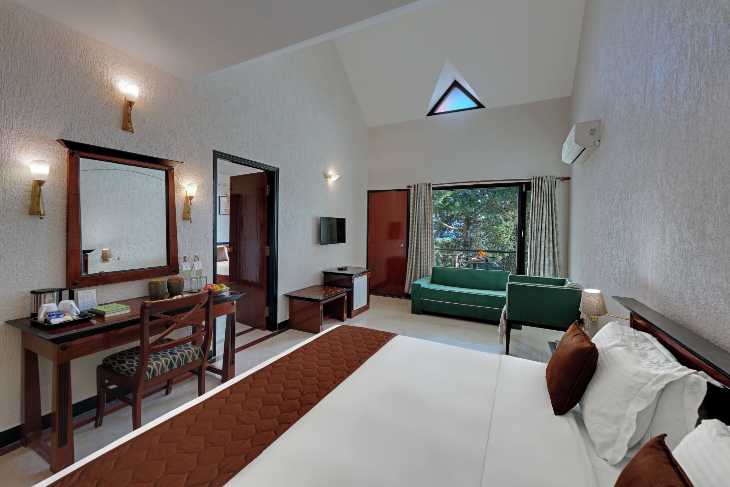 Una habitación de hotel con una cama grande, un escritorio con una silla, un sofá verde y un televisor montado en la pared.