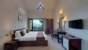 Quarto de hotel com cama, escrivaninha, televisão e varanda com vista.