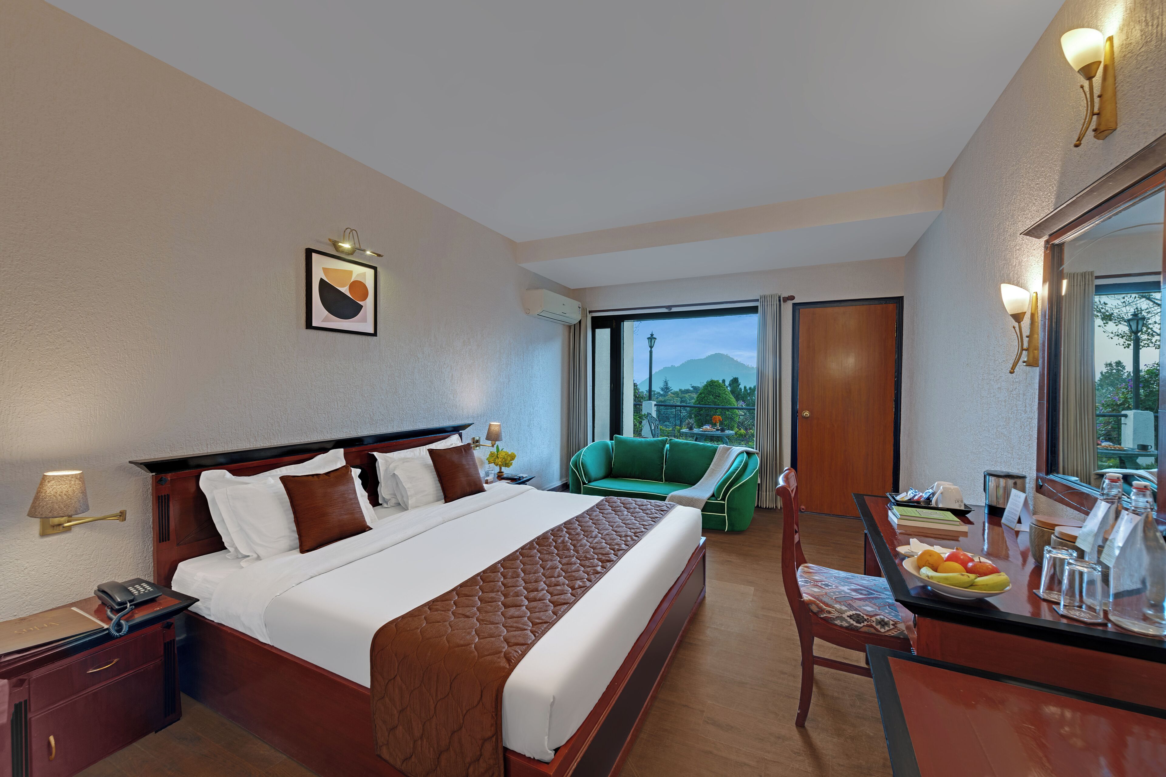 Een hotelkamer met een bed, een groene bank, een eettafel met fruit, en uitzicht op het landschap.