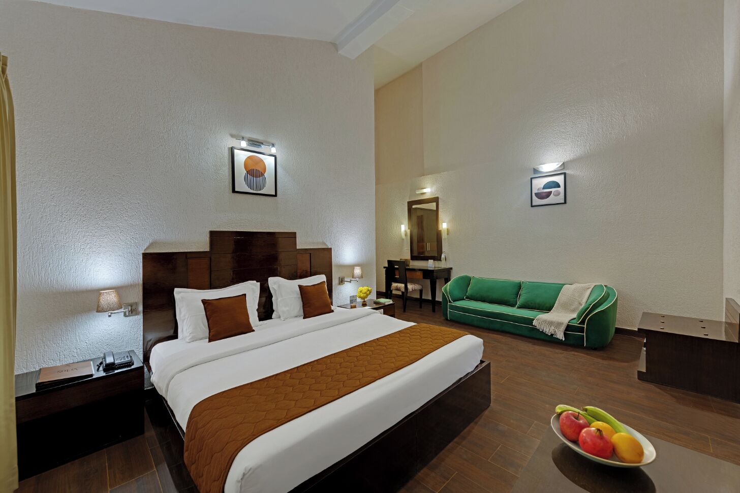 Una habitación de hotel con una cama grande, un sofá verde, un escritorio y un frutero.