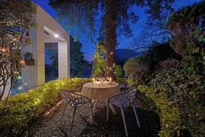 An outdoor dining area with a round table and chairs, surrounded by greenery and decorative lights. - 8fold-Pinecrest By LaRiSa, Bhimtal (Nainital)