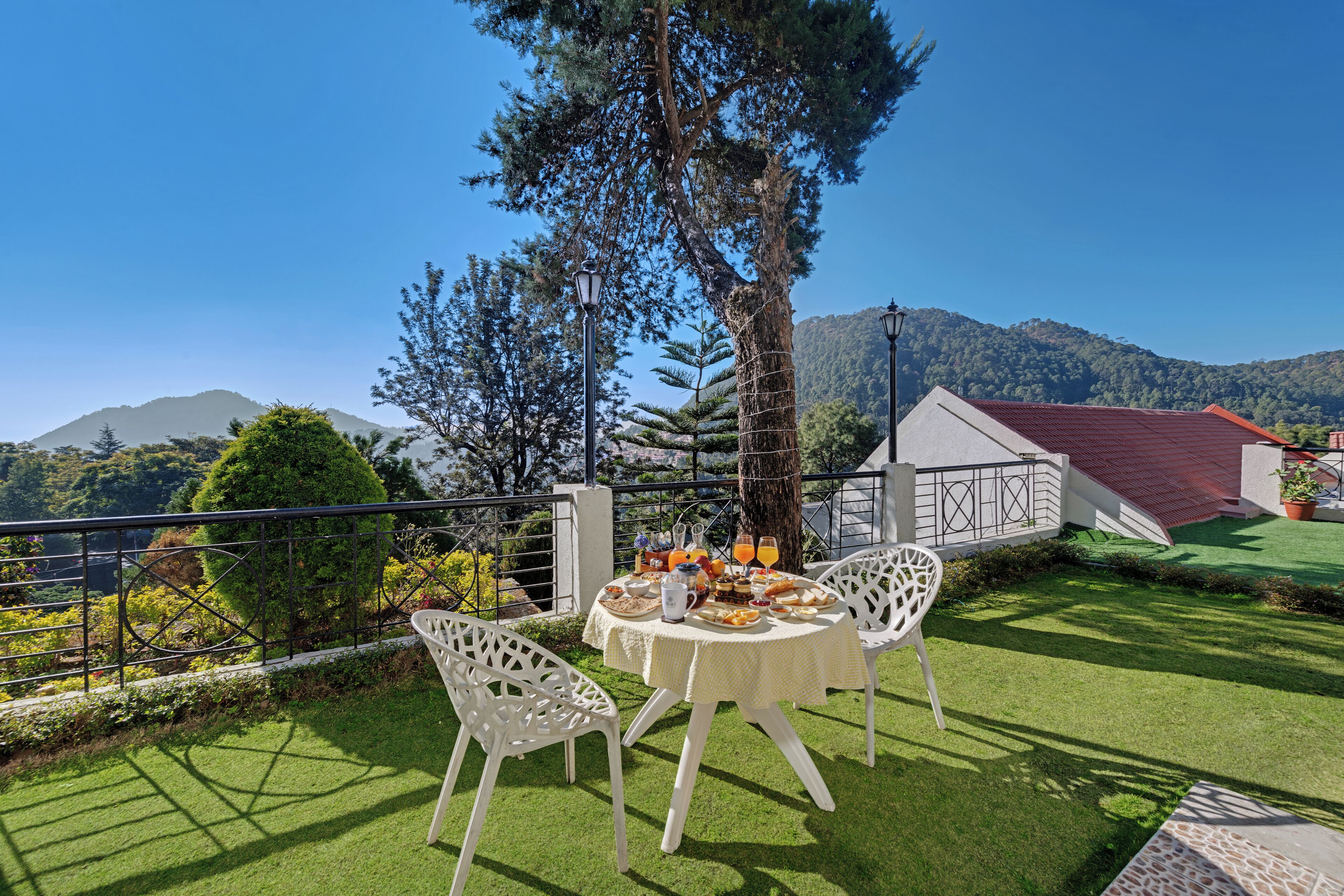 An outdoor dining area with a table set for two, surrounded by greenery and a view of a mountain.