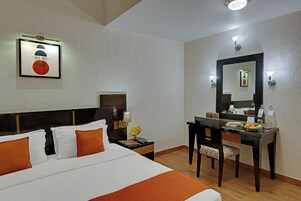 A hotel room with a large bed, a desk with a chair, a nightstand, and a mirror.