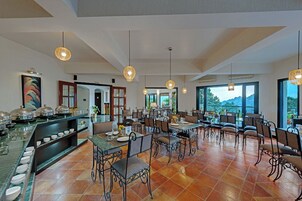 Un amplio comedor con mesas y sillas altas, un mostrador de buffet con platos, y grandes ventanales que ofrecen vistas al exterior.
