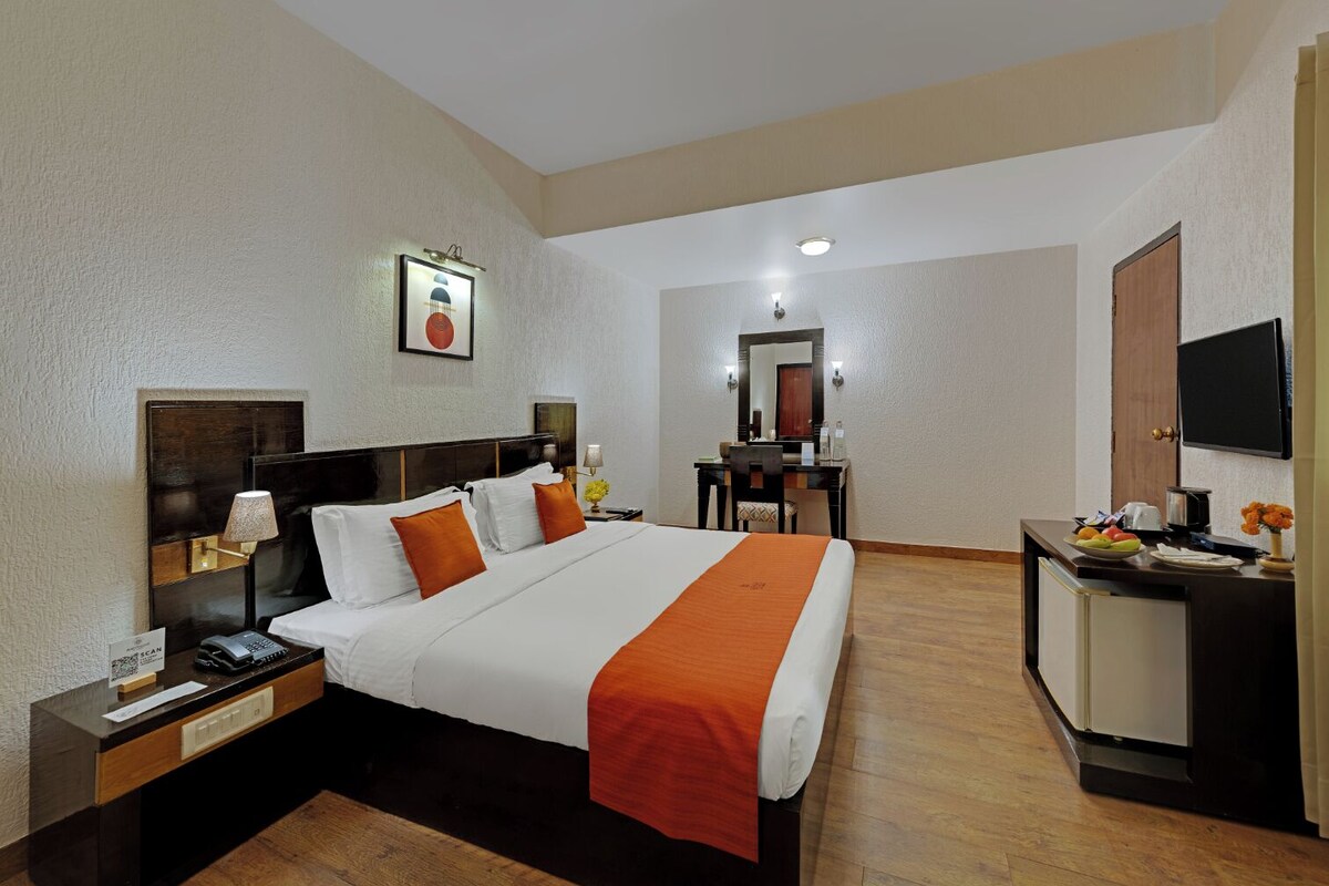 A hotel room with a large bed, a desk with a chair, a television, and a mirror.