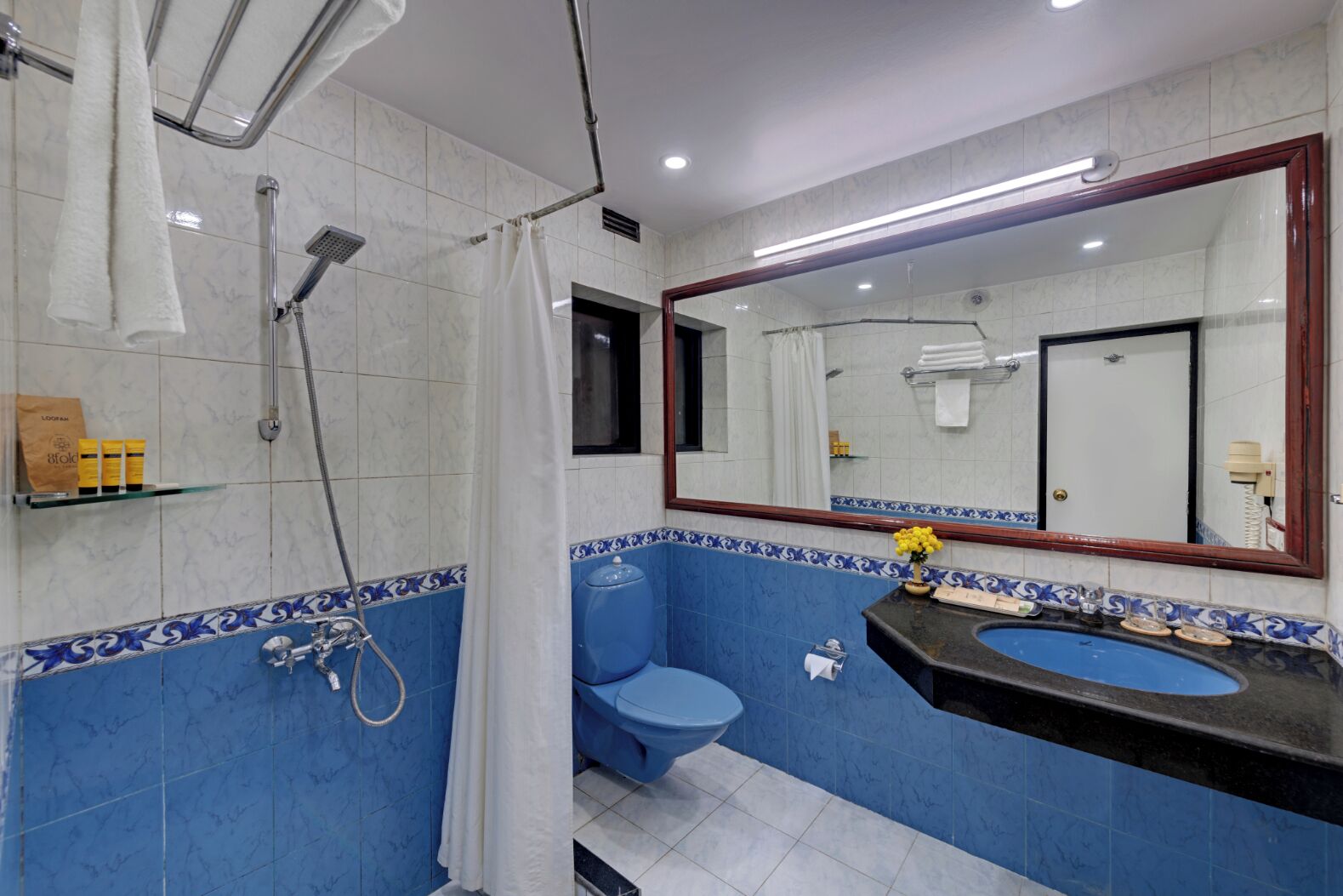 A bathroom with a blue and white tiled wall, a white shower curtain, a blue toilet, a black sink with a mirror above it, and a towel rack with a white towel.