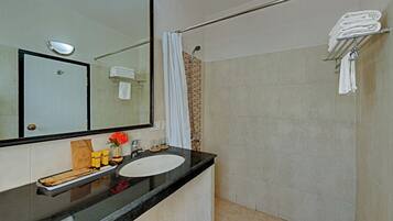 A bathroom with a black countertop, white sink, and a large mirror. There is a shower curtain, a towel rack, and a small shelf with toiletries.