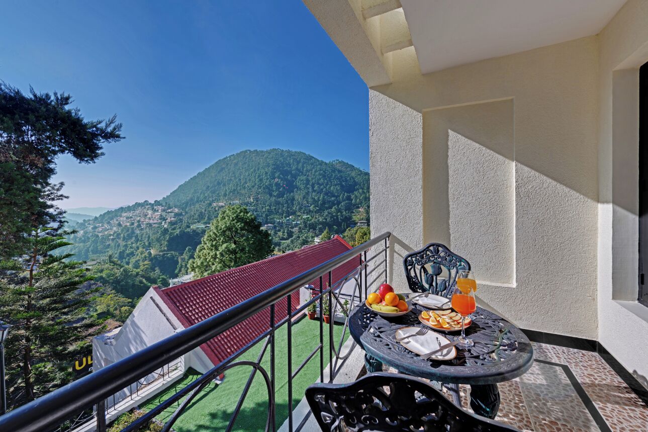 A balcony with a table set for breakfast, overlooking a mountainous landscape.
