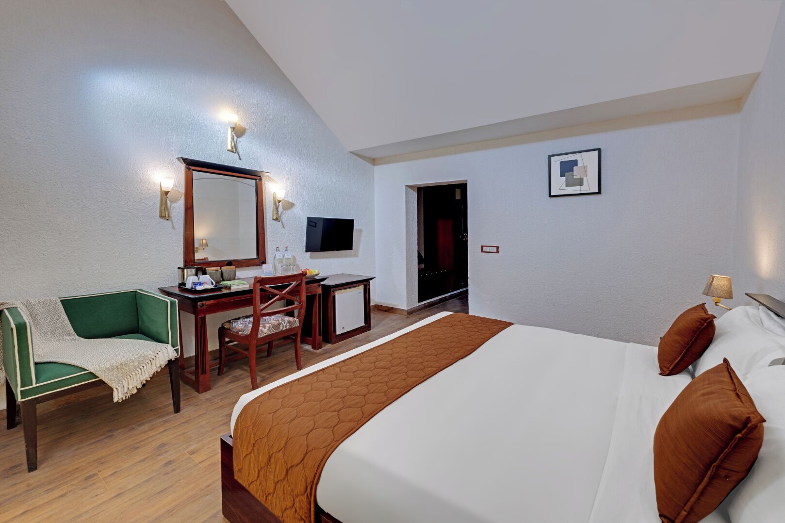 Habitación de hotel con cama, escritorio, silla, televisor y puerta.