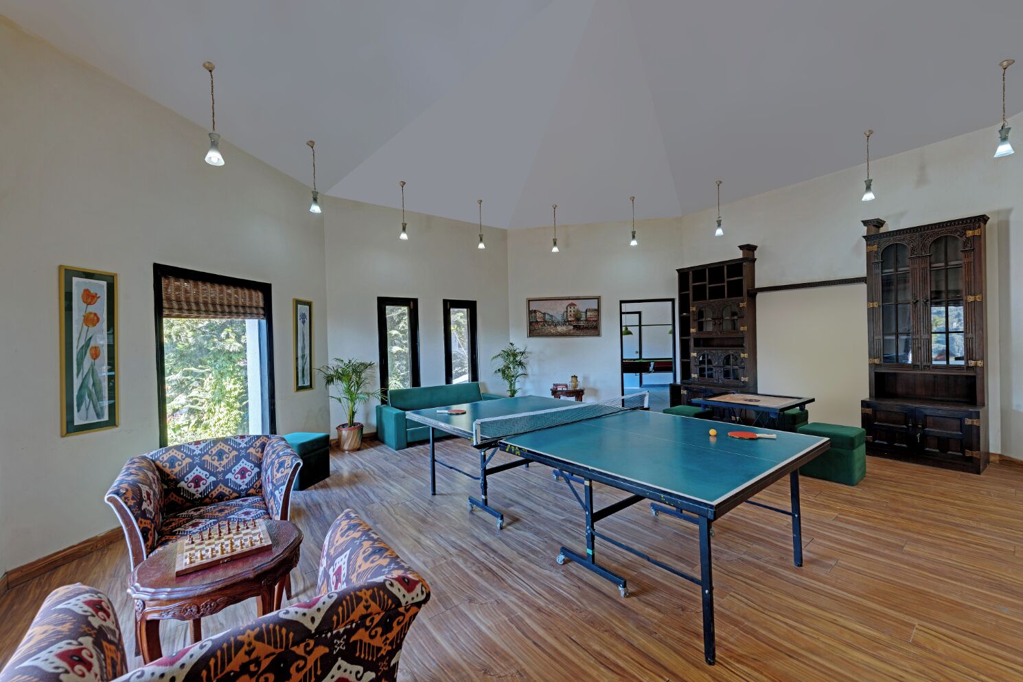 A spacious room with a ping pong table, a sofa, and a chess table. There are multiple windows and a large cabinet.