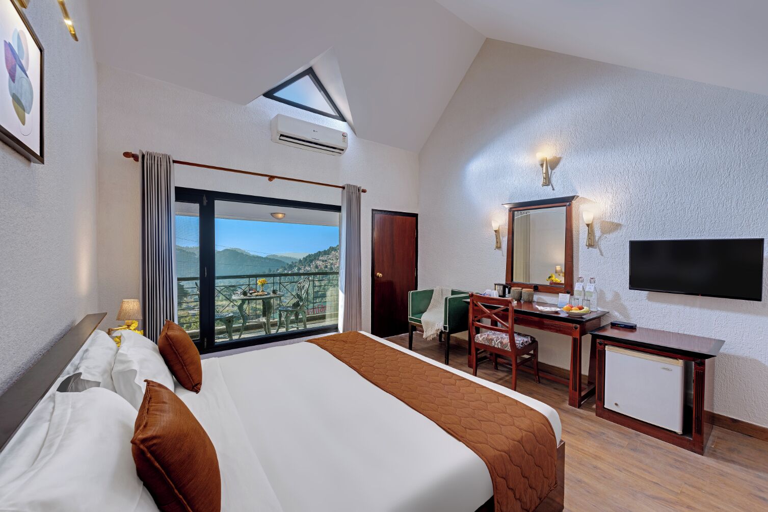 Habitación de hotel con una cama grande, un escritorio, una silla, un televisor y un balcón con vistas a la montaña.