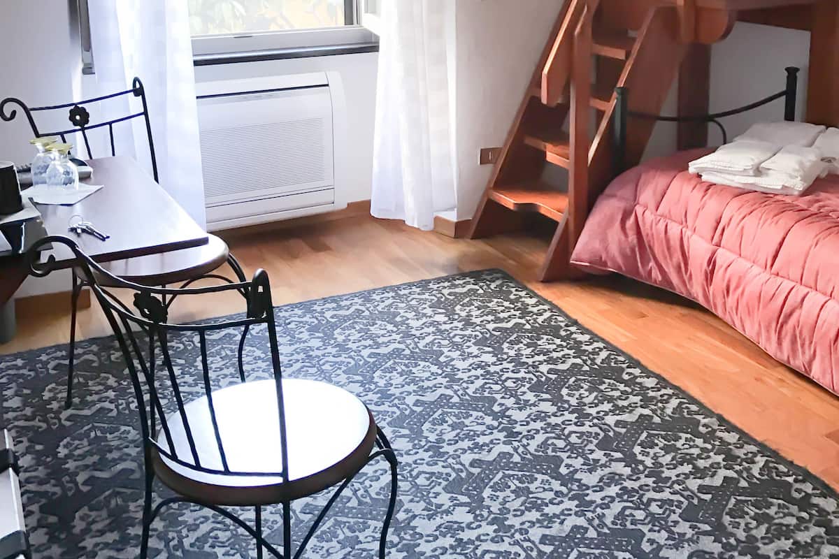 Un dormitorio con una escalera de madera, una cama con una manta rosa, un escritorio con una silla y una ventana con cortinas.