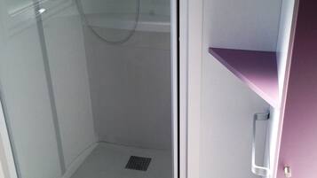 A glass-enclosed shower with a handheld showerhead, a small white trash bin, and a purple shelf unit.