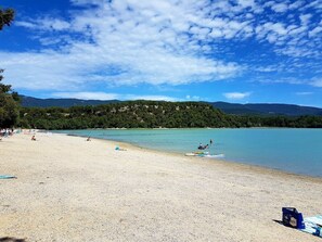 A beach with clear water, a sandy shore, and a forested hill in the background. - Camping de la Bonde (Cabrieres-d'Aigues)