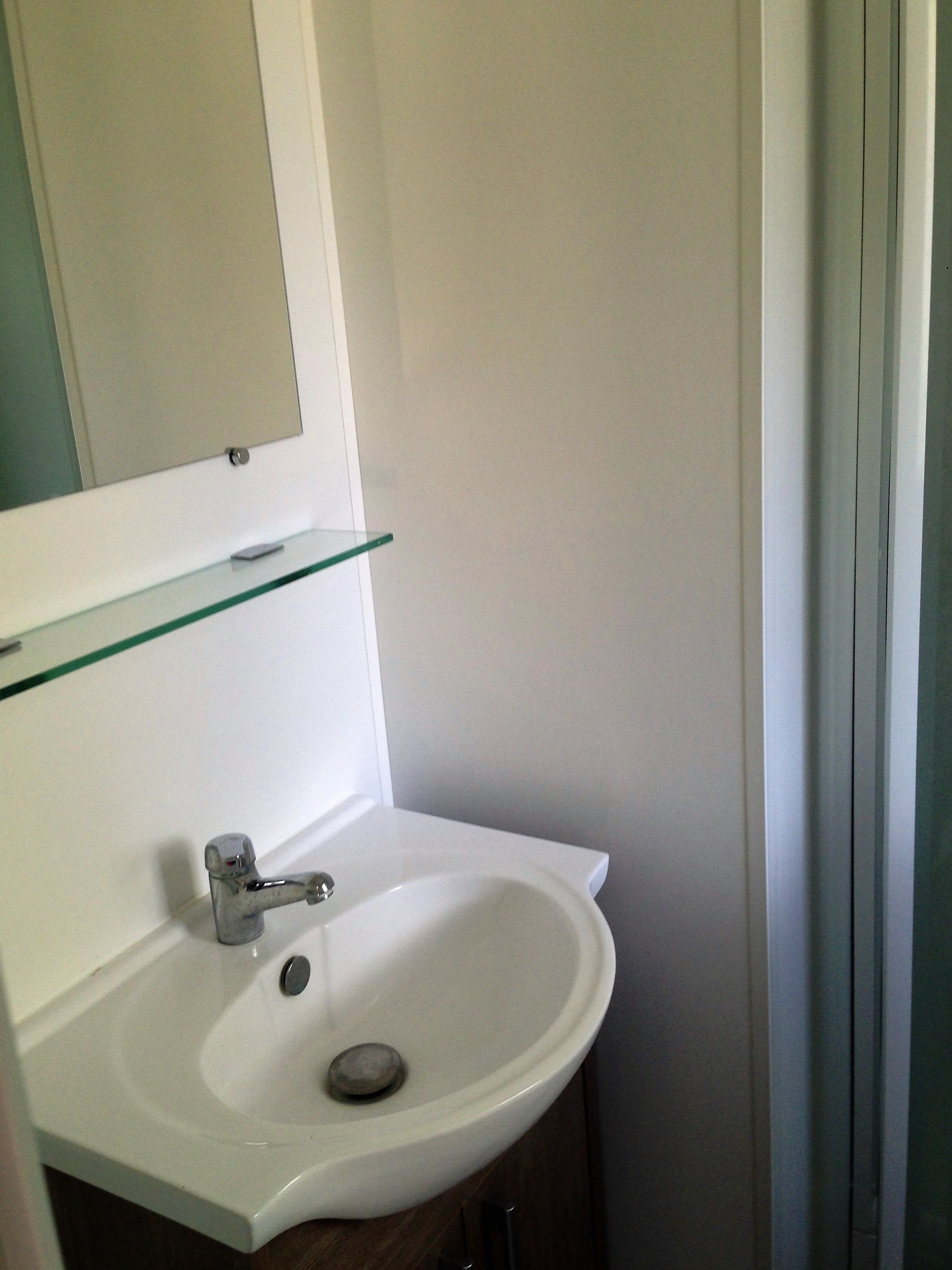 A bathroom with a white sink, a glass shelf above it, and a mirror above the shelf.