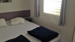 Una habitación de hotel con cama, almohadas, una mesita de noche, una ventana con cortinas y una lámpara de pared.
