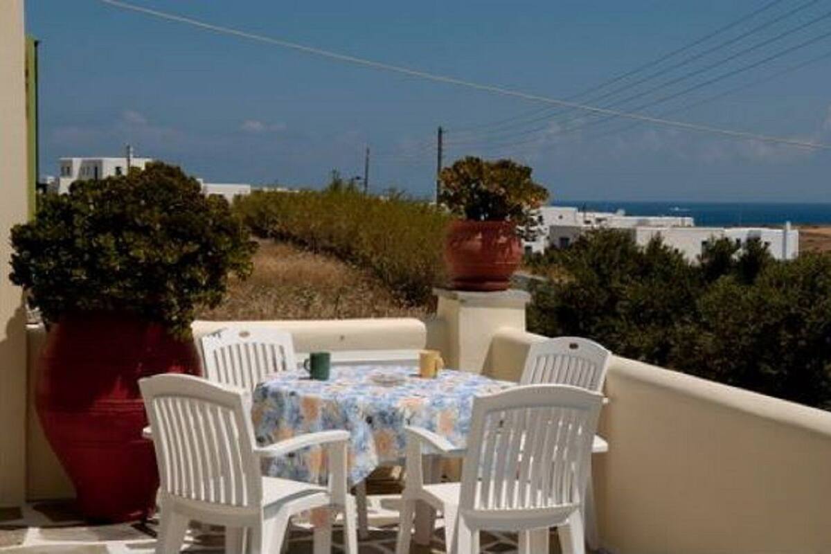 A balcony with a table and chairs, overlooking a coastal area with buildings and a clear sky.