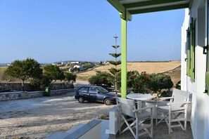 A terrace with a view of a coastal landscape, a parked car, and outdoor seating. - Asante Paros (Paros)
