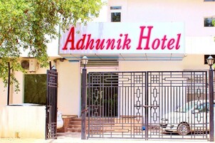 Exterior del hotel Adhunik con un letrero llamativo, una entrada con portón y un coche estacionado.
