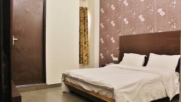 Un dormitorio con estructura de cama de madera, ropa de cama blanca, pared con estampado floral y una puerta cerrada.