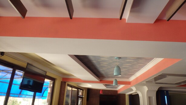 A room with a ceiling featuring a geometric pattern, a visible television, and a door leading to another room. - Mau Summit Hotel (Narok)