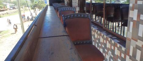 A covered outdoor seating area with rows of chairs and a long table.