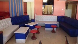 A modern lounge area with blue and white sofas, red stools, and a central table. - Mau Summit Hotel (Narok)