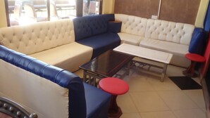 A seating area with a sofa, a small table, and a red stool. - Mau Summit Hotel (Narok)