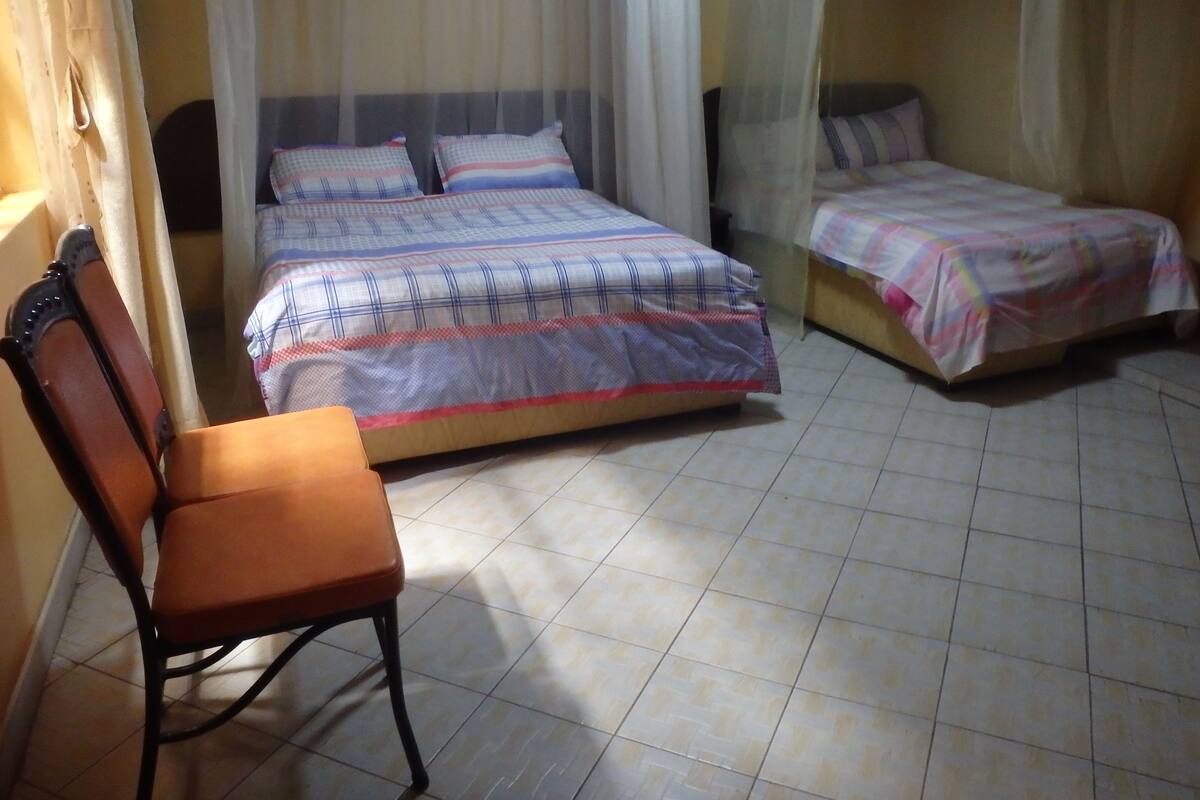 A bedroom with two beds, a chair, and a mosquito net.