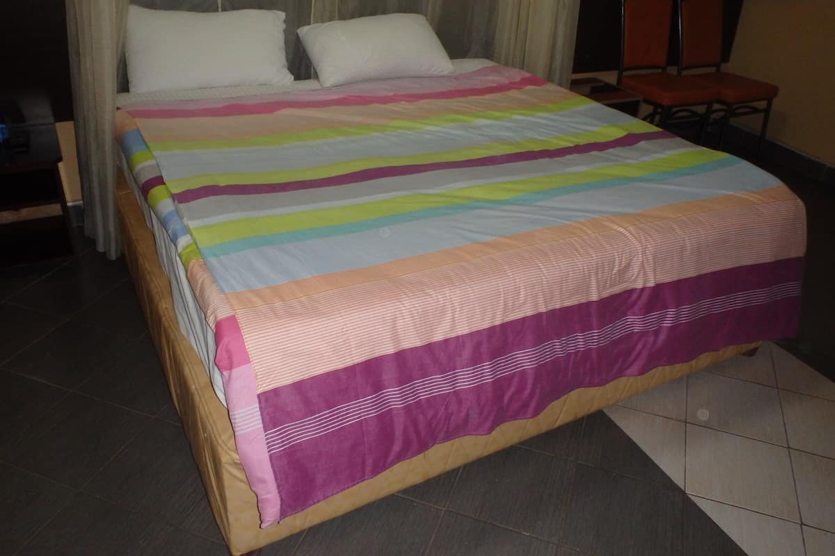 A bed with a colorful striped bedspread, a wooden headboard, and a chair in the corner.