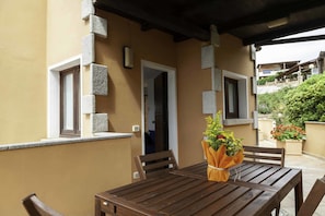 A wooden table with chairs and a bouquet of flowers on a balcony with a beige wall and stone accents.
