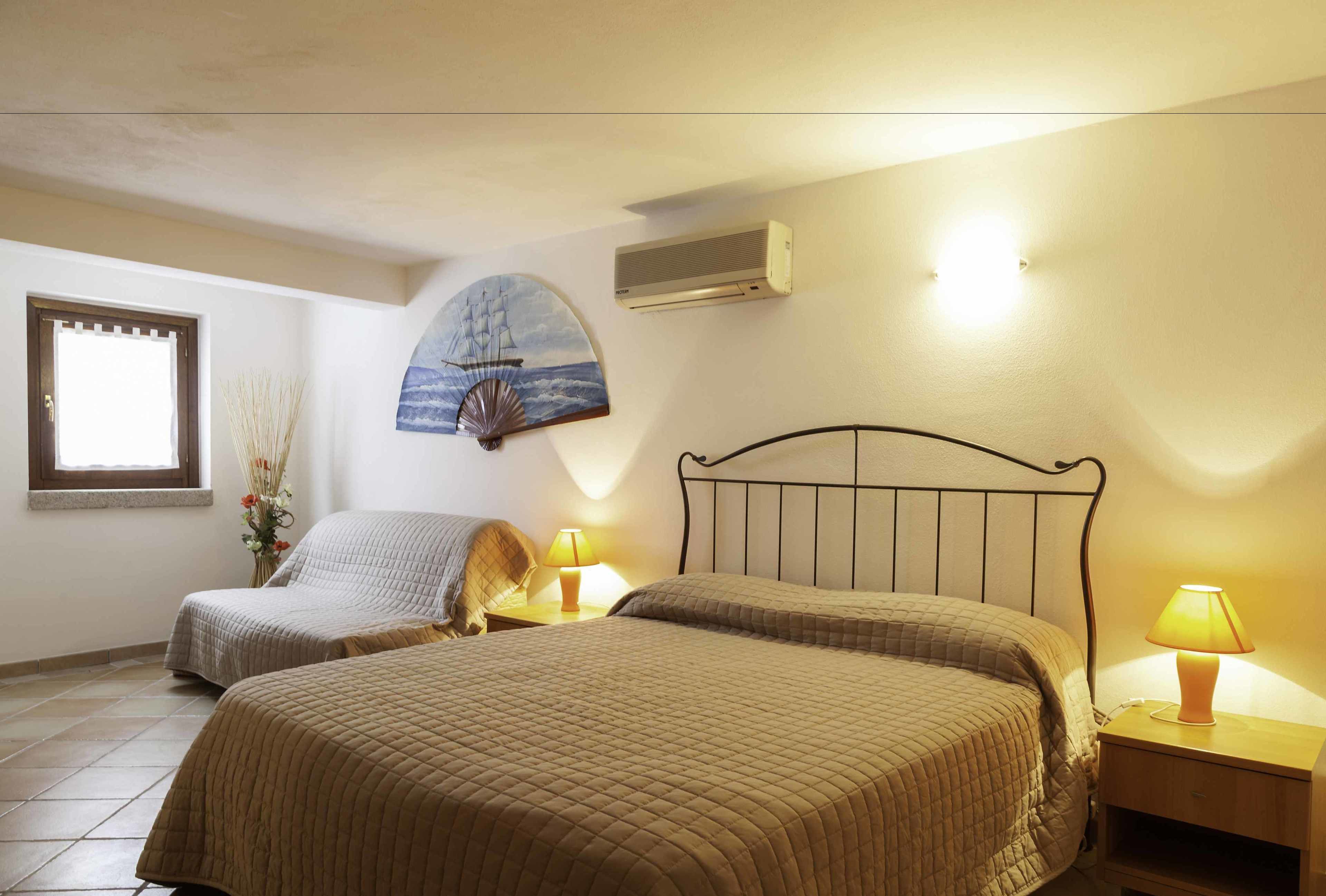 A bedroom with two beds, a wall-mounted air conditioner, and a decorative ship painting.