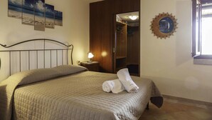 A neatly made bed with a quilted bedspread, a bedside lamp, and a wall with a framed artwork.
